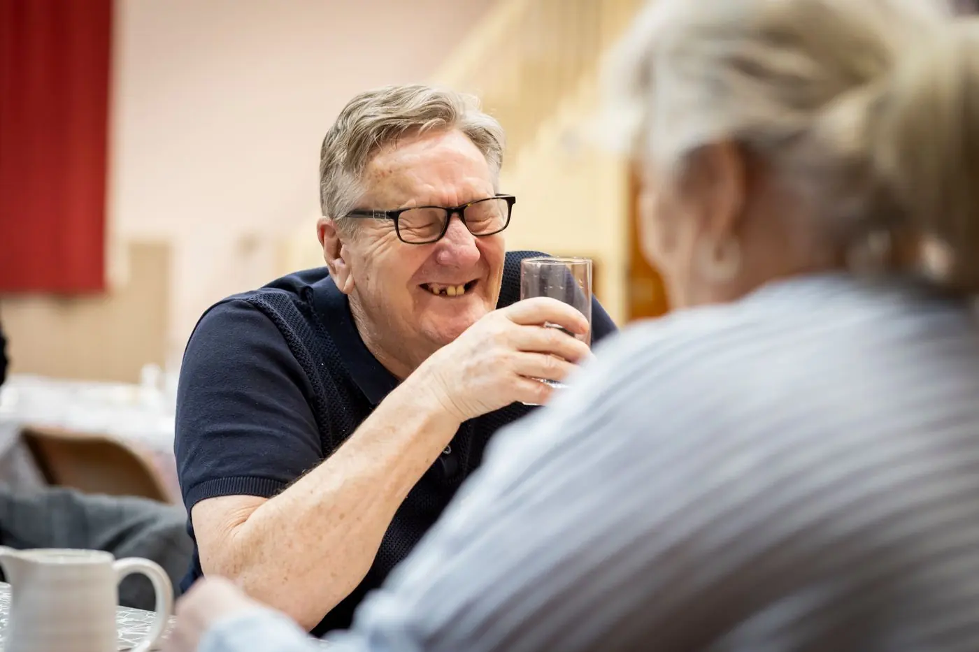 An older man laughing with a companion over a drink