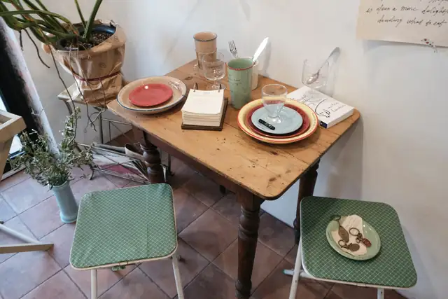 A small table set with plates beside a window, with two green chairs