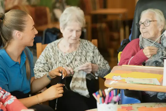 A carer sitting with two older women as they knit