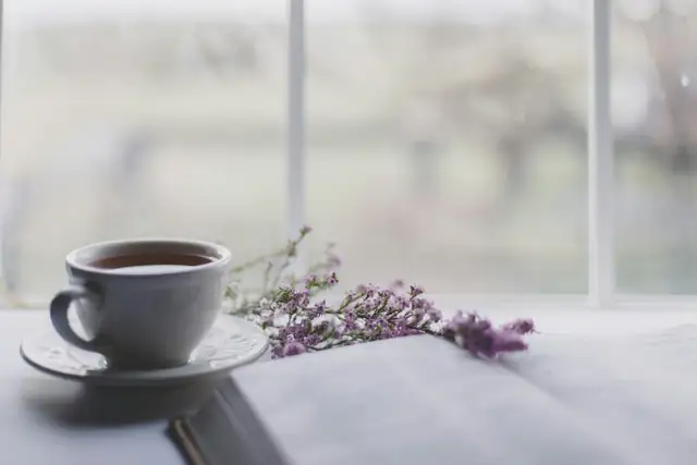 A cup of tea and a sprig of lavender on a table by a bright window