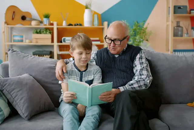 A grandfather reading a book with his grandson on the couch