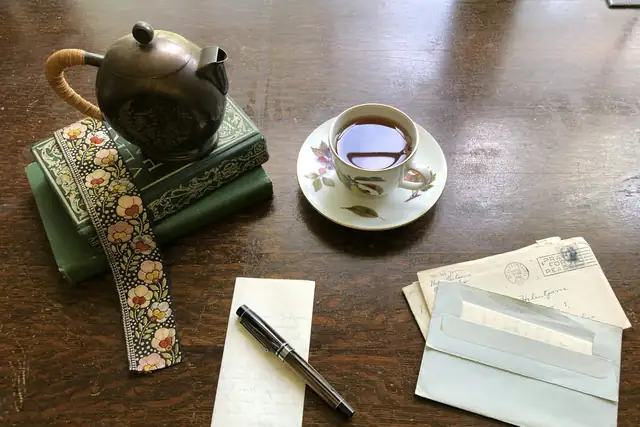 A teapot and a cup of tea beside books, letters and a pen