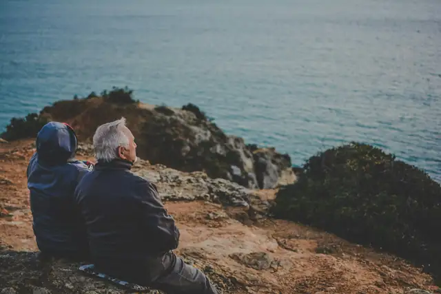 Two people sitting together on rocks, looking out to sea