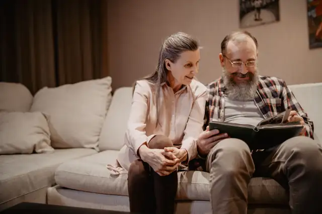 An older couple smiling together on the sofa as they look through a photo album