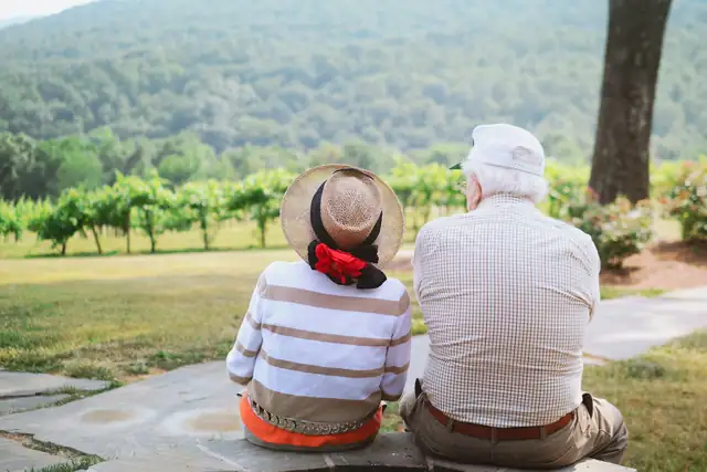 An older couple sitting together on a path, looking out over green hills