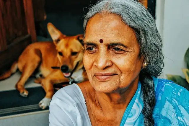An older woman with long grey hair sitting beside her dog