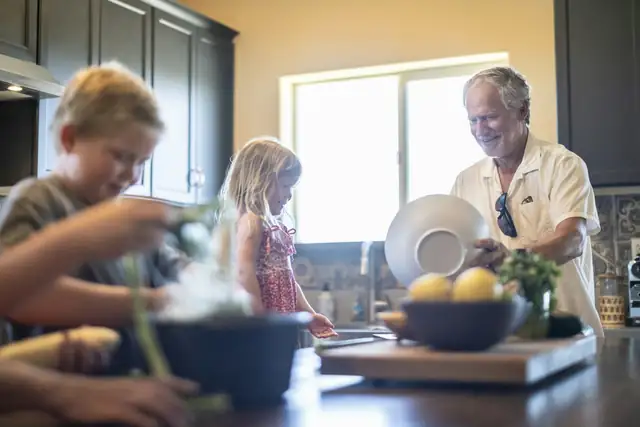 A grandfather cooking in a sunny kitchen with his grandchildren