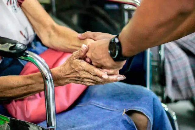 A man holding the hands of an older woman sitting in a wheelchair