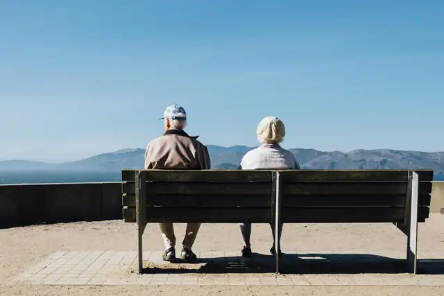 An older couple sitting together on a bench facing the sea
