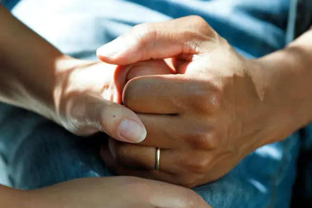 Two hands held together, one wearing a gold wedding band