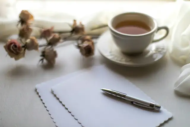 A cup of tea beside writing paper, a pen and dried roses